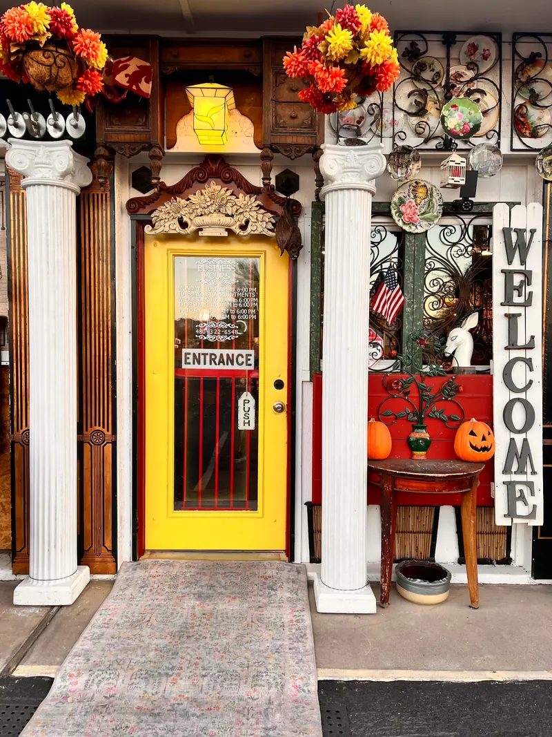The yellow entrance door of Sample Studios Art & Antiques between white columns, with a Welcome sign