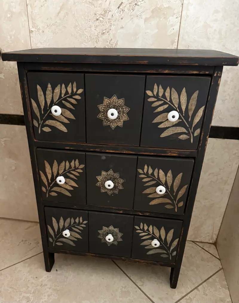 A black cabinet hand-painted with leaves, with white porcelain knobs