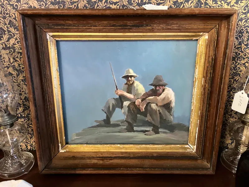 An oil painting of two men resting on a hillside, in a gilt frame at Sample Studios